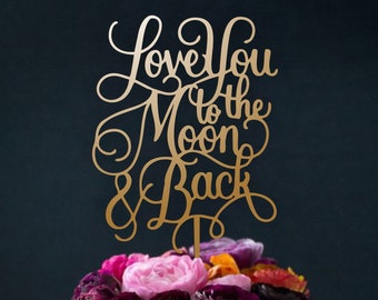May include: A chocolate cake with a brown frosting and a gold topper that says "Love You to the Moon & Back". The cake is decorated with pink and purple flowers.