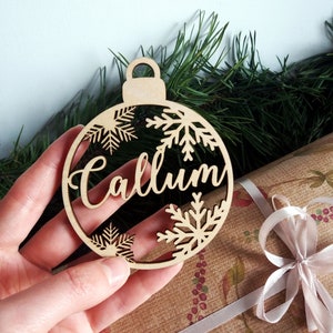 May include: A wooden Christmas ornament shaped like a bauble with the name "Callum" cut out in the center. The ornament is decorated with snowflake cutouts.