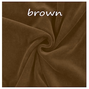Op de afbeelding: Een stuk bruine fluwelen stof met een zachte, matte textuur en zichtbare plooien die natuurlijke schaduwen cre&euml;ren. Het woord brown is in witte, kleine, schreefloze letters bovenaan in het midden van het stofoppervlak gedrukt.