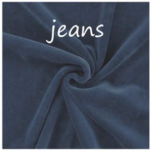 Op de afbeelding: Een donkerblauwe fluwelen stof met een zachte, pluche textuur en een wervelend draperingspatroon. Het woord jeans is in witte, kleine, schreefloze letters in het midden bovenaan de stof gedrukt, wat contrasteert met de diepblauwe kleur.