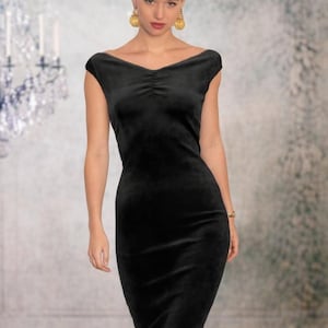 Op de afbeelding: Een zwarte fluwelen jurk met een brede, off-shoulder halslijn en een subtiel geplooid detail in het midden aan de voorzijde. Het kledingstuk is getailleerd bij de romp en taille en loopt uit in een rechte, knielange rok met korte mouwen.