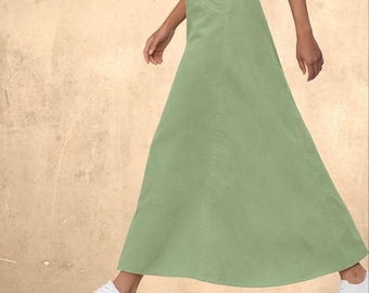 Op de afbeelding: Een saliegroene maxirok met een hoge taille, knoopsluiting, een voorzak en een lang, vloeiend silhouet dat tot de enkels reikt, gecombineerd met strakke witte sneakers voor een eenvoudige en functionele uitstraling.