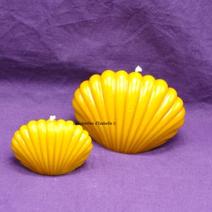 Puede incluir: Dos velas de cera amarilla con forma de conchas. La concha más grande mide aproximadamente 15 cm de ancho y la más pequeña aproximadamente 10 cm de ancho.