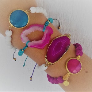 May include: Four bracelets with different gemstone and bead accents. The bracelets feature a white lava rock, a pink agate, a blue agate, and a pink agate with a gold accent.