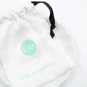 May include: White drawstring bag with a black ribbon tie. The bag has a green circle with the initials "LM" and the text "LISA MAXWELL" printed on it.