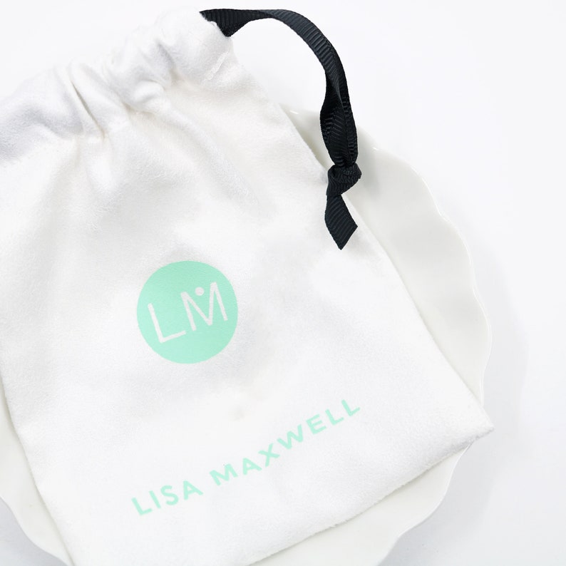 May include: White drawstring bag with a black ribbon tie. The bag has a green circle with the initials "LM" and the text "LISA MAXWELL" printed on it.