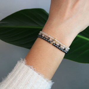 May include: Three layered bracelets with black and clear beads and gold accents. The bracelets are stacked on a person's wrist.