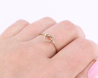 May include: A gold heart-shaped knot ring. The ring is thin and delicate, and the knot is a simple, elegant design.