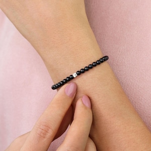 May include: A black beaded bracelet with a silver bead accent. The bracelet is worn on a person's wrist.