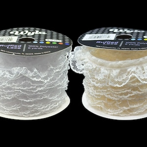 May include: Two spools of ruffled lace in white and cream. Each spool is labelled with the brand "Wyla" and contains 5.49 metres of 100% polyester lace. The lace has a delicate, scalloped edge.