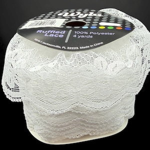 May include: A roll of white ruffled lace made from 100% polyester. The label states "Ruffled Lace" and "4 yards". The lace features a delicate, openwork pattern and is suitable for various craft projects.