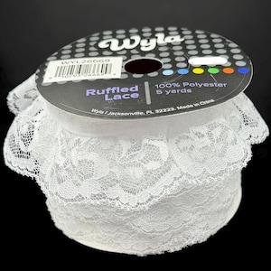 May include: A roll of white ruffled lace. The label reads "Wyla" and "Ruffled Lace". The spool contains 4.57 metres of 100% polyester lace. The lace is a delicate, openwork design, ideal for sewing and crafting projects.