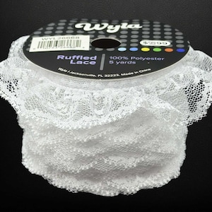 May include: A roll of white ruffled lace. The label reads "Ruffled Lace" and "100% Polyester 5 yards". The lace has a delicate, open weave with a scalloped edge. The spool is black with a white and grey label.