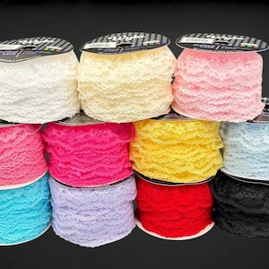May include: Ten spools of ruffled lace in a variety of colours, including white, cream, pink, red, and black. Each spool is neatly stacked, showcasing the delicate texture and vibrant hues of the lace. The lace is made of polyester.
