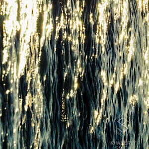 May include: Abstract photograph of water with a rippling surface reflecting sunlight. The water is a deep blue color and the sunlight creates a shimmering effect.