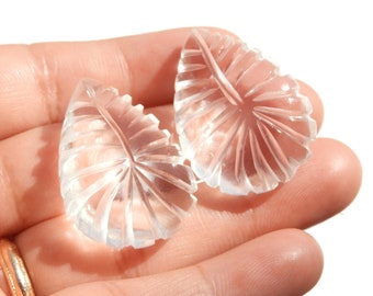 Puede incluir: Dos hojas de cristal de cuarzo transparente con un diseño tallado. Las hojas se sostienen en una mano.