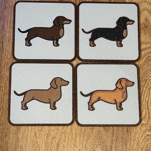May include: Set of four square coasters featuring dachshund dog illustrations in various colors: brown, black, tan, and orange. Each coaster has a white background with a brown border, perfect for protecting surfaces from drink rings.