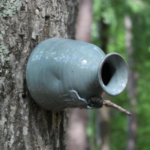 May include: A blue ceramic birdhouse attached to a tree trunk. The birdhouse has a round opening for birds to enter.