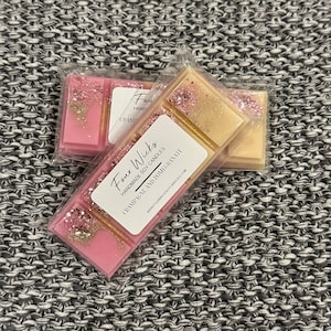 May include: Two pink and gold wax melts with the text "Four Wicks Handmade Soy Candles Champagne and Pomegranate www.fourwicksoycandles.com" on the packaging.