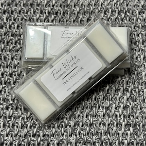 May include: Four Wick Soy Candles in a clear plastic packaging with a silver label that reads "Four Wicks Handmade Soy Candles Mod Vanilla Type" and a website address. The candles are white and have a silver glitter accent.