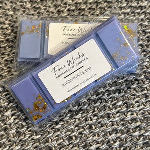 May include: A close-up of a lavender soy wax melt with gold glitter. The wax melt is packaged in a clear plastic bag with a white label that reads "Four Wicks Handmade Soy Candles" and "Wonderstruck Type". The label also includes the website address "www.fourwicksoycandles.com".