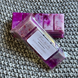 May include: A set of four wax melts in clear plastic packaging. The wax melts are purple and white with glitter. The packaging has a label that says "Four Wicks Handmade Soy Candles Iced Summer Berries www.fourwicksoycandles.com"