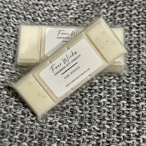 May include: A white wax melt with a light pink shimmer. The wax melt is packaged in a clear plastic bag with a white label that reads "Four Wicks Handmade Soy Candles Baby Powder www.fourwickssoycandles.com"