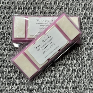 Könnte beinhalten: Zwei Wachsschmelzen in transparenter Verpackung. Die Wachsschmelzen sind rosa und weiß und haben vier Dochte. Die Verpackung hat ein Etikett mit der Aufschrift "Four Wicks Handmade Soy Candles Pink Cloud Type www.fourwicksoycandles.com"
