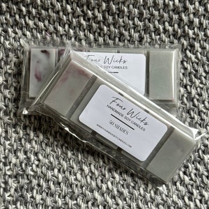 May include: Two packs of grey and white soy wax melts with the text "Four Wicks Handmade Soy Candles 50 Shades www.fourwickssoycandles.com" on the front.