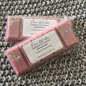 Könnte beinhalten: Zwei rosa Sojawachs-Schmelzen mit Glitzer, verpackt in durchsichtigem Plastik. Das Etikett lautet "Four Wicks Handmade Soy Candles" und "Flower Bomb Type".
