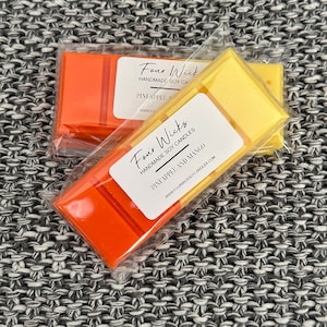 May include: Two wax melts in clear packaging. The top melt is yellow and says "Four Wick Handmade Soy Candles Pineapple" and the bottom melt is orange and says "Four Wicks Handmade Soy Candles Pineapple and Mango".