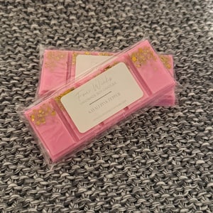 May include: Two pink wax melts with gold glitter, labelled "Four Wicks Handmade Soy Candles" and "Kawa Kawa Pink Pepper".