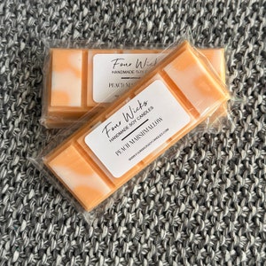 May include: Two wax melts in clear packaging. The wax melts are peach and white and have a swirl design. The label says "Four Wicks Handmade Soy Candles Peach Marshmallow www.fourwickssoycandles.com"