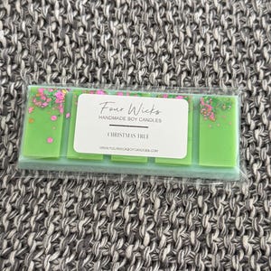Puede incluir: Un paquete de ceras de soja hechas a mano en un envoltorio transparente. Las ceras son de color verde brillante y están decoradas con chispas rosas y verdes. La etiqueta dice "Four Wicks Handmade Soy Candles" y "Christmas Tree".