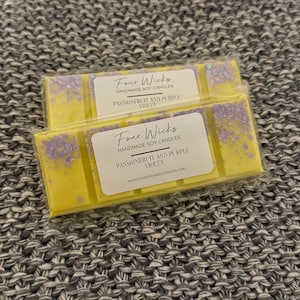 May include: Two yellow wax melts with a purple glitter design. The wax melts are labelled "Four Wicks Handmade Soy Candles Passionfruit and Purple Violet" and "WWW.FOURWICKSOYCANDLES.COM".