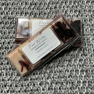 Könnte beinhalten: Eine Packung mit vier Docht-Sojawachskerzen im Duft "Caramel Latte" der Marke "Four Wicks Handmade Soy Candles". Die Verpackung ist weiß mit schwarzem Text und einem braunen und weißen Wachs-Schmelzstück im Inneren.