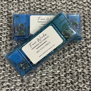 May include: Two wax melts in clear packaging. The wax melts are blue with glitter and have a label that says "Four Wicks Handmade Soy Candles Dive Into Cypress www.fourwicksoycandles.com".