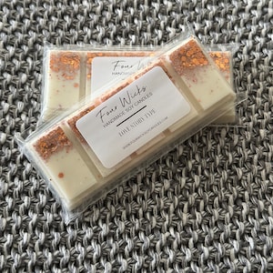 May include: Soy wax melt bars in clear packaging. Each bar has a white base with copper glitter accents. The label reads "Four Wicks Handmade Soy Candles LOVE STORY TYPE". The background is a grey knitted fabric.