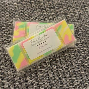 May include: A pack of four soy wax melts in a clear plastic wrapper. The wax melts are in a swirl pattern of pink, yellow, and green. The pack has a white label with the text "Four Wicks Handmade Soy Candles" and "Fruit Tingles" with the website address "www.fourwickssoyscandles.com".
