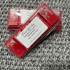 May include: Two red wax melts with glitter in clear packaging. The label reads "Four Wicks Handmade Soy Candles Dill. Desire. Type. www.fourwickssoycandles.com"