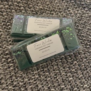 May include: Two green soy wax melts with glitter, packaged in clear plastic. The label reads "Four Wicks Handmade Soy Candles Rivergum www.fourwicksoycandles.com"