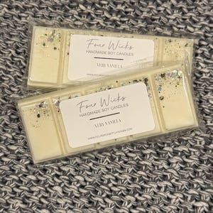 May include: Two rectangular wax melts in clear packaging, labeled "Four Wicks Handmade Soy Candles, Very Vanilla." The wax is a creamy off-white color, speckled with glitter. The background is a gray and white knitted fabric.