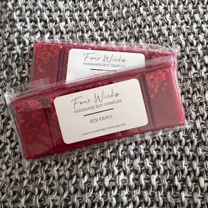 May include: Two packs of red wax melts, labelled "Four Wicks Handmade Soy Candles." The melts are a deep red colour with glitter accents. The label also reads "Red Frogs" and the website address.