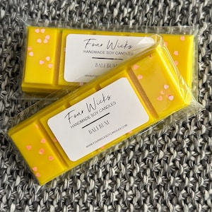 May include: Two yellow soy wax melts with pink hearts, packaged in clear plastic. The label reads "Four Wicks Handmade Soy Candles Bali Bum www.fourwicksoycandles.com"