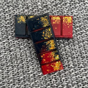May include: Two wax melts, one black with gold glitter and one red with gold glitter. Both are divided into six sections.