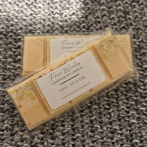 May include: A close-up of a wax melt bar with gold glitter. The bar is labelled "Four Wicks Handmade Soy Candles" and "Saint - Vond Type".