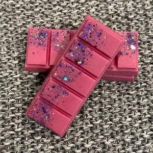 May include: A pink wax melt with purple glitter. The wax melt is in a six-cube tray and is stacked on top of another wax melt.