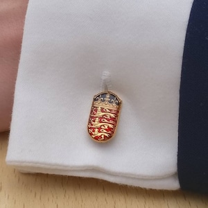 Puede incluir: Gemelos de oro con un diseño de esmalte rojo, blanco y azul que presenta una corona y un escudo de armas.