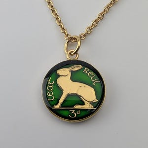 Peut inclure: Un collier doré avec un pendentif circulaire sur fond émaillé vert. Le pendentif présente un lièvre doré au centre, avec le texte 'leat' à gauche, 'Reul' à droite et '3d' en bas, le tout inscrit en lettres dorées sur le pourtour.