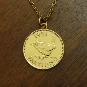Könnte beinhalten: Goldkette mit einem Anhänger aus einer britischen Farthing-Münze von 1951 mit einem Zaunkönig. Die Münze hat einen perlenbesetzten Rand und das Wort "Farthing" ist um den Vogel herum eingeschrieben.